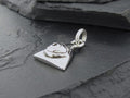 Silver heart-shaped charm with a small clasp on a dark stone surface.