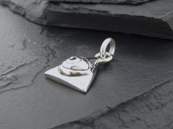Silver heart-shaped charm with a small clasp on a dark stone surface.