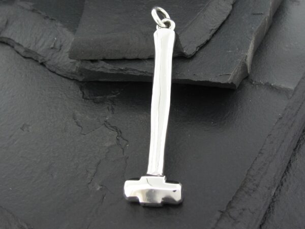 Small silver hammer pendant on a textured dark surface.