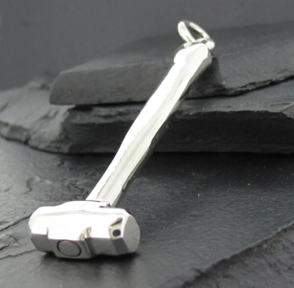 A silver pendant shaped like a hammer on a dark surface.