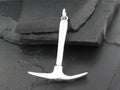 Silver pickaxe pendant on a dark stone surface.