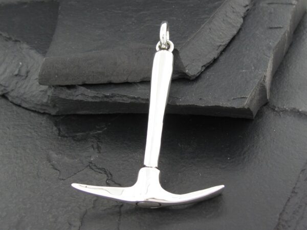 Silver pickaxe pendant on a dark stone surface.