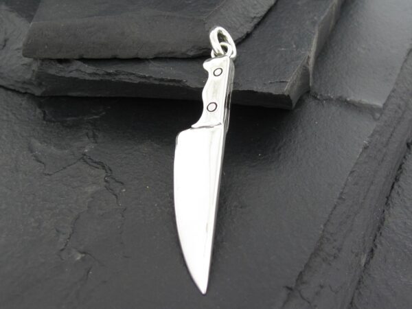 A silver knife pendant on a dark surface.