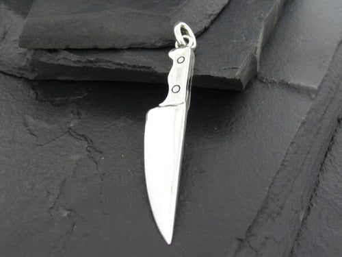 A silver knife pendant on a dark surface.