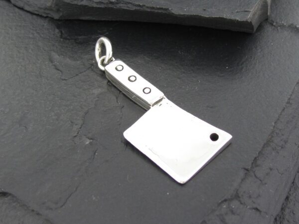 Silver cleaver-shaped pendant with rivet details on dark surface.