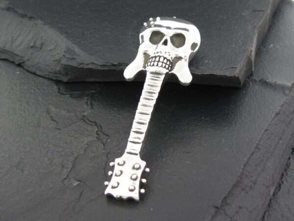 Metal guitar pendant with a skull design on top, placed on a dark stone surface.