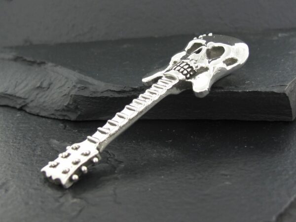 A guitar-shaped pendant with skull details on a black surface.