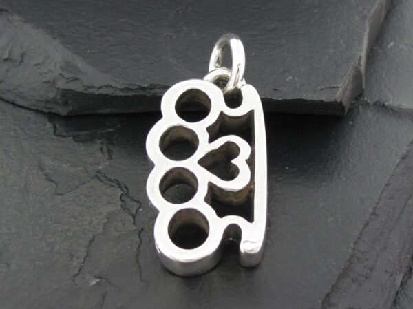 Silver pendant shaped like brass knuckles with heart detail.