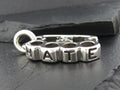 Close-up of a silver pendant spelling 'NATIE'.