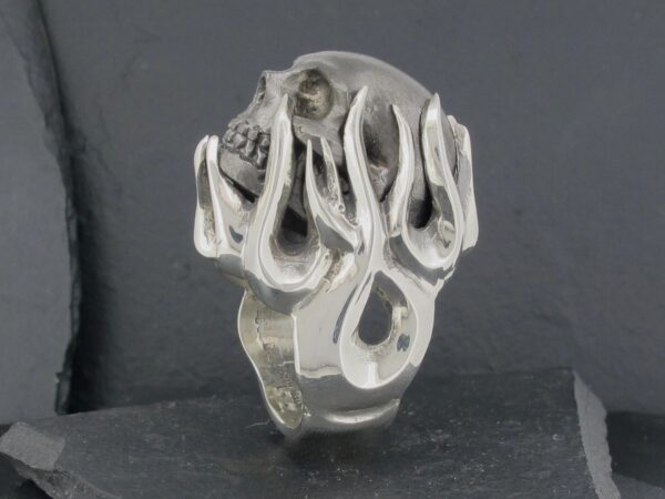 Silver ring with a skull and abstract design on a dark background.