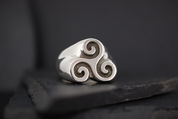 Silver ring with a triple spiral design on a dark surface.