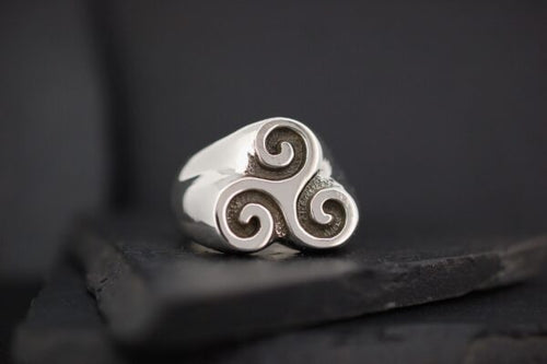 Silver ring with a triple spiral design on a dark surface.