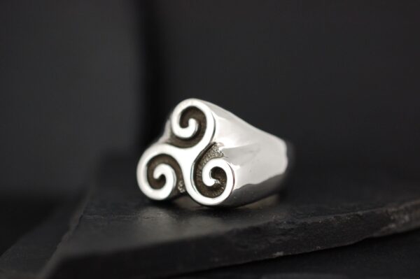 A silver ring with a triskelion design.