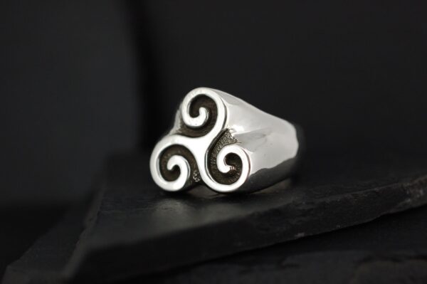 Silver ring with a triskelion design on a black background.