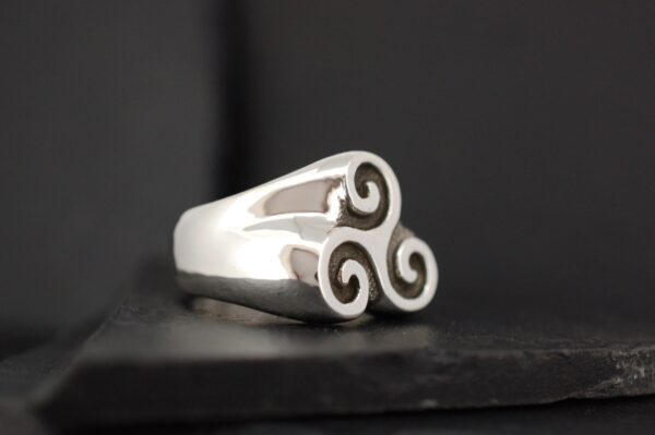 Silver ring with a triskelion design on a dark background.