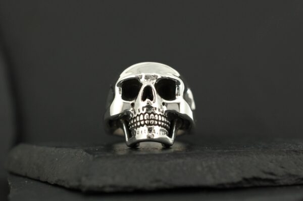 A polished silver skull ring on a dark surface.