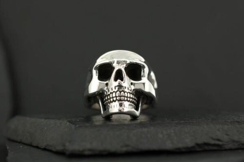 A polished silver skull ring on a dark surface.