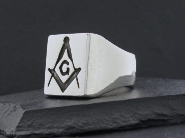 Silver ring with a black Masonic symbol on a gray background.