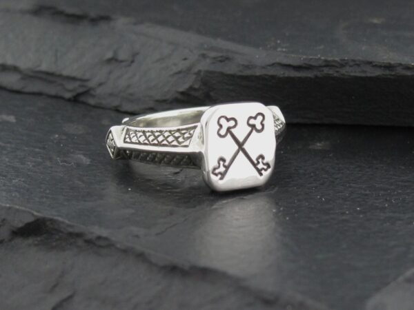 Silver ring with crossed keys engraved on its square face.