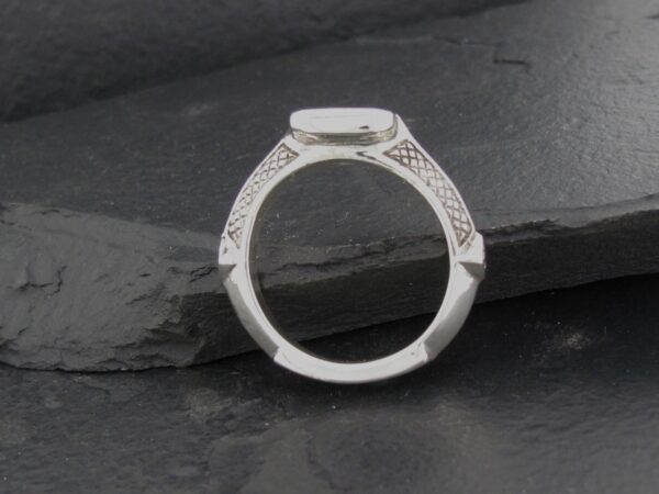 Elegant silver ring with intricate side detailing on a dark stone background.