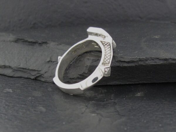 Silver ring with intricate geometric design on dark surface.