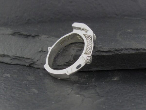 Silver ring with intricate geometric design on dark surface.
