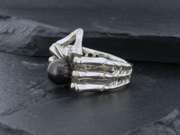 Silver ring with a black pearl on dark stone background.