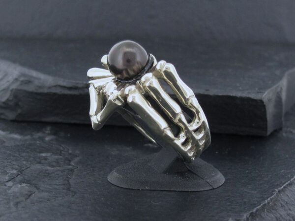 Silver ring with a black stone and a unique skeletal design.