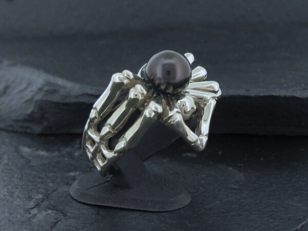 A silver spider-shaped ring with a black pearl on top.