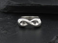 Silver infinity symbol ring on a dark surface.