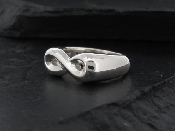 Sleek silver infinity symbol ring on a dark surface.