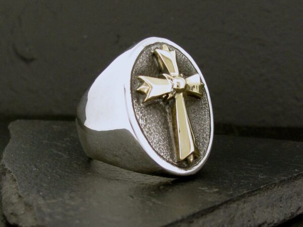 A silver ring with a gold cross on an oval face.