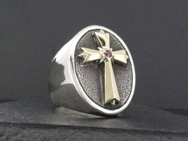 Silver ring with a cross and red gemstone centerpiece.