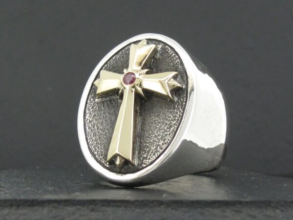 Silver ring with a raised cross and a central red gem.