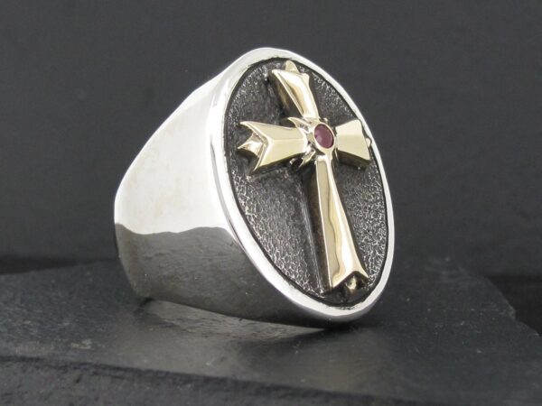 Silver ring with a gold cross and red gem.