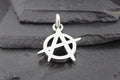 Silver anarchy symbol pendant on a dark textured background.
