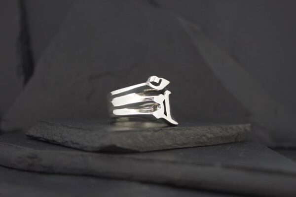Silver ring with a unique geometric design on a black surface.