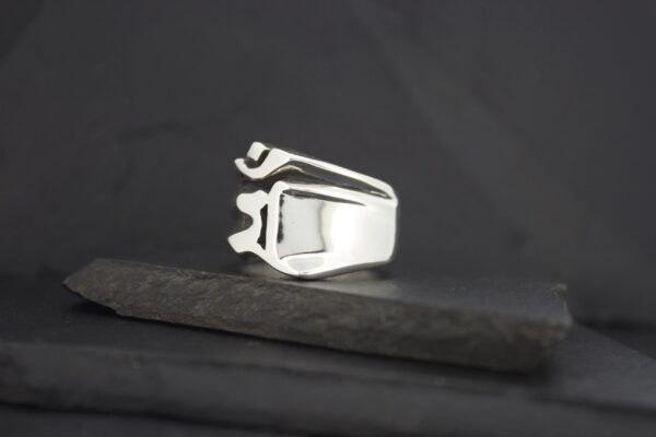 A shiny silver ring with a modern geometric design on a dark surface.
