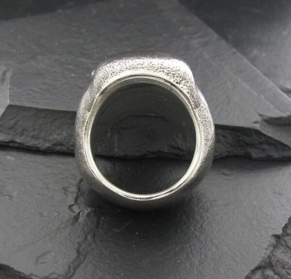 A silver ring with intricate designs on a dark textured surface.