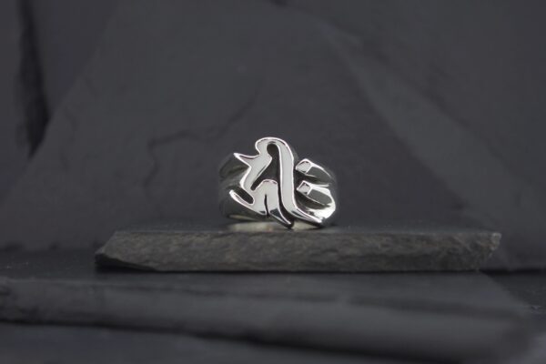 Silver ring with a gothic-style letter design on a dark surface.