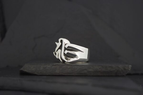 A silver ring with a unique, artistic design on a dark surface.