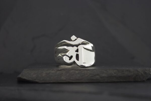 Silver ring with a raised Om symbol on a dark background.