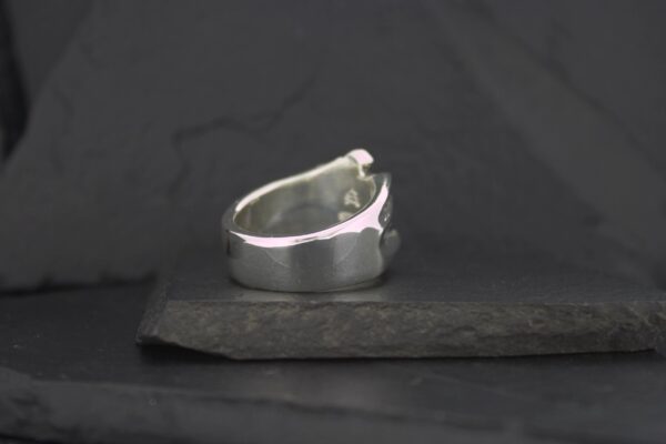 A silver ring with a jagged design on a dark surface.