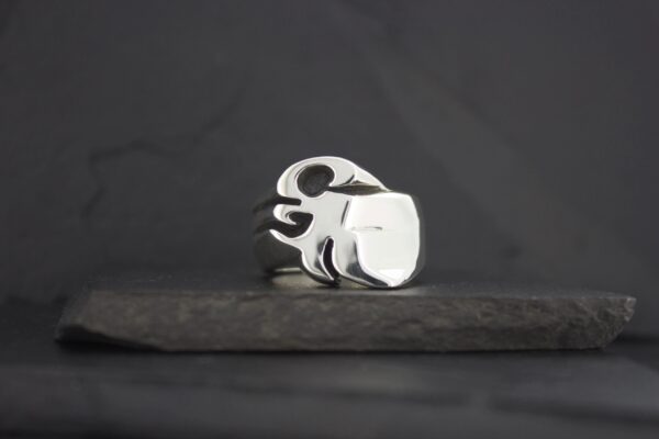 Silver ring with a flame design on a dark surface.