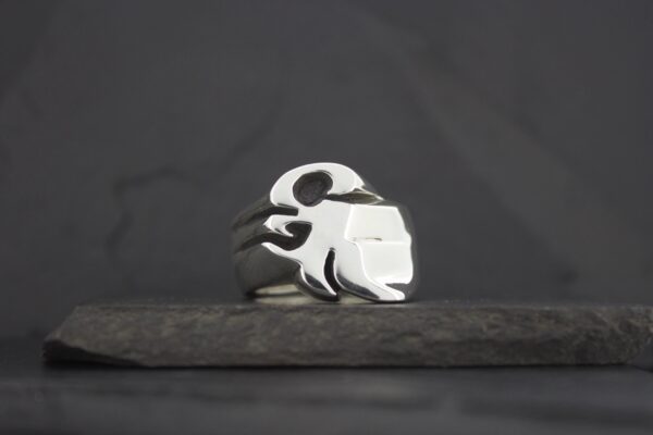 A silver ring with a skull design on a dark surface.