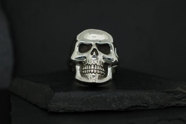 A silver skull ring displayed on a black cushion.
