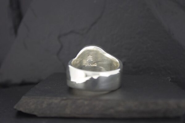 Silver ring with an irregular, hammered design on a dark background.