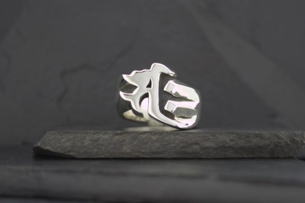 Silver ring with a gothic letter design on a dark surface.