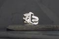 Silver ring with a gothic letter design on a dark surface.