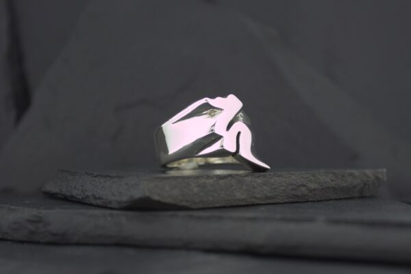 A silver ring featuring a stylized, abstract human figure design.